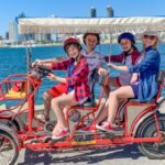 Family riding in a red six person surrey rented from Wheel Fun Rentals on Coronado Island. San Diego skyline in the backdrop
