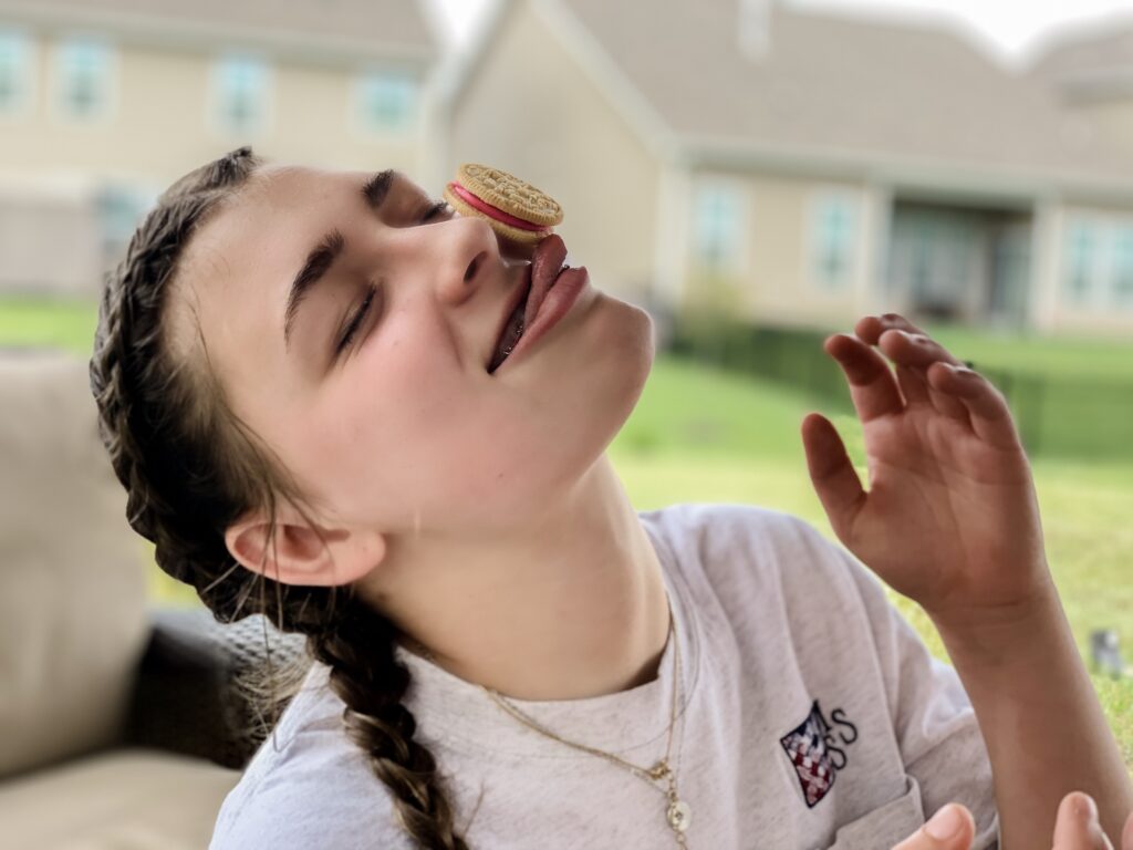 Girl balances oreo on her face as she plays minute to win it game. - Safe Summer Bucket List – 100 Ways to Have Fun This Summer While Social Distancing