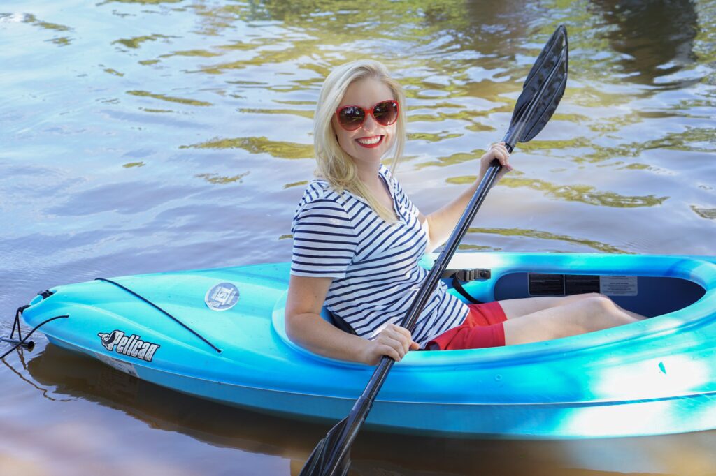 Woman in blue kayak paddles through a river. - Safe Summer Bucket List – 100 Ways to Have Fun This Summer While Social Distancing