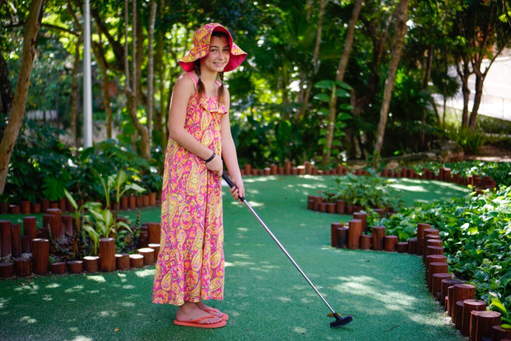 Girl pictured playing putt-putt golf. playing putt-putt golf could be a great way to get out of the house with kids while social distancing. Just be sure to wait your turn for each hole and keep a good pace. - Safe Summer Bucket List – 100 Ways to Have Fun This Summer While Social Distancing