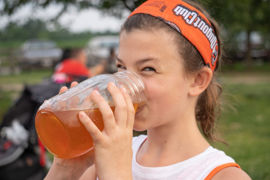 Girl sips iced tea from a mason jar. Cool off with some refreshing lemonade or an iced tea. Try a few mocktails (no alcohol needed), a root beer float or use a shaved ice machine and flavored syrups to create yummy snow cones. - Safe Summer Bucket List – 100 Ways to Have Fun This Summer While Social Distancing