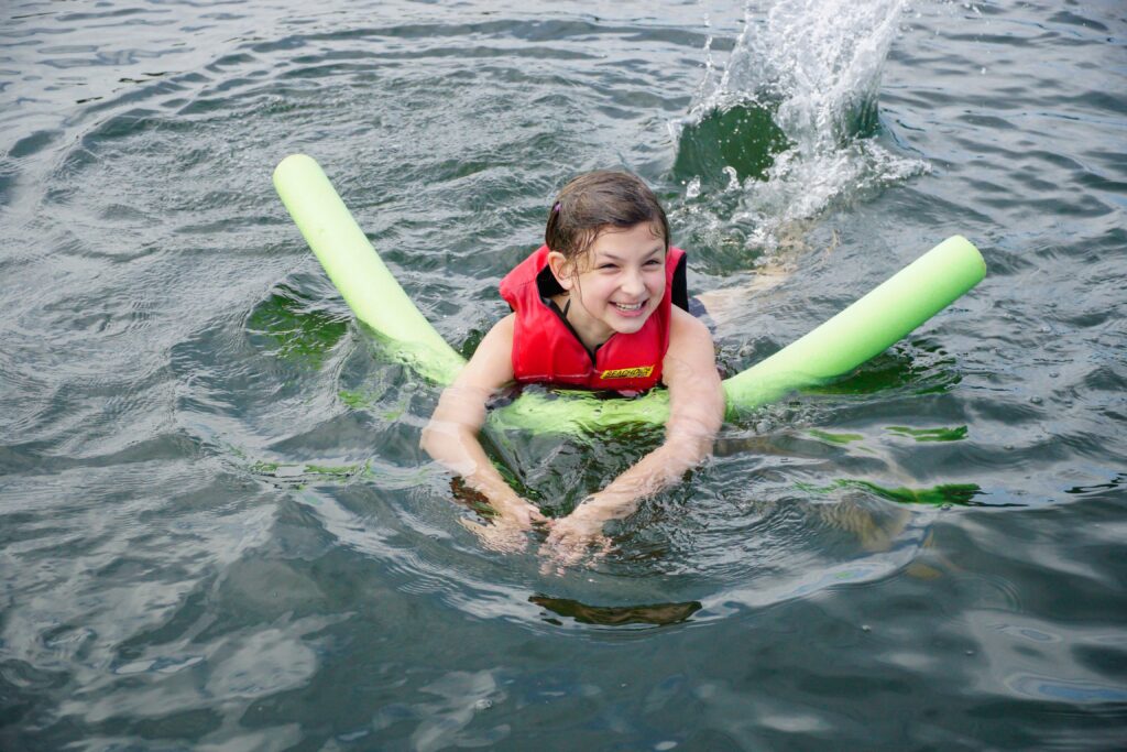 Girl swims in a swimming lake as water splashes around her. Even if your local neighborhood pool or rec center isn’t open yet chances are you can find a local lake or swimming hole where you can jump in an cool off away from a crowd. 