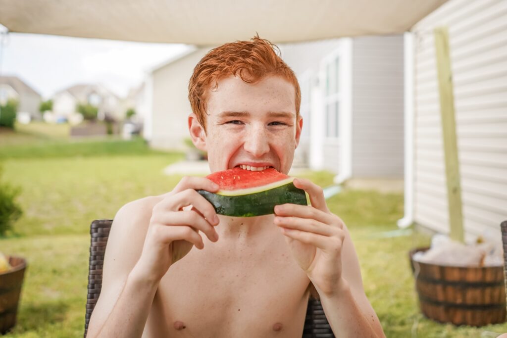 Teenage boy eating slice of watermelon. Another treat synonymous with the season is fresh watermelon. See who can eat the most of this juicy treat without using or who can eat a slice the fastest. 