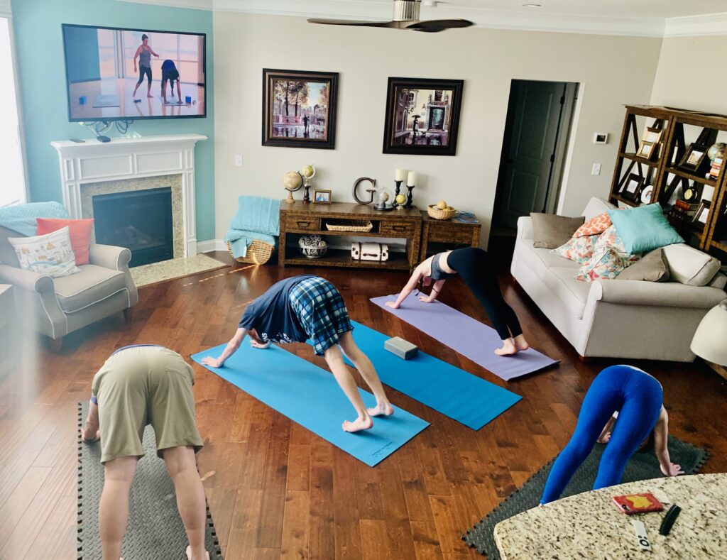 Family practicing yoga on mats in living room of house. Clear your couches to the side and lay down some yoga mats and start your day off with some movement and mindfulness.