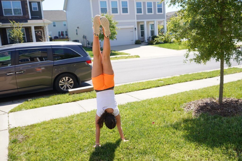 Girlpractices hand stand on the lawn in front of home. earn to cartwheel and flip this summer on a trampoline or on the lawn. Solid gymnastics skills can take weeks to fully perfect so make sure you are on hand to spot and supervise. 