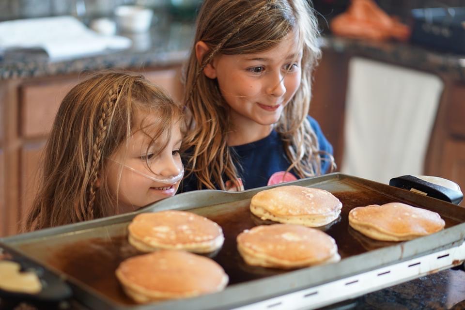 Young girls eye pancakes in the griddle with delighted expectation. Whether it’s trying out Eggs Benedict or making a big pile of pancakes on the griddle, it can be fun to change things up and surprise the kids! 