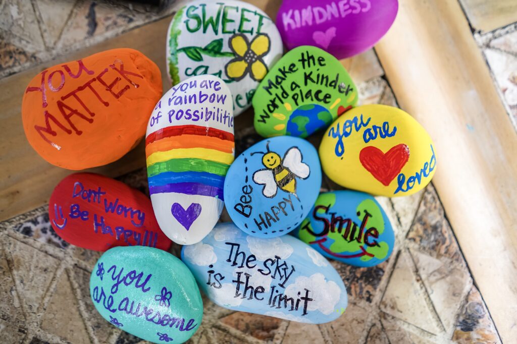 Pile of rocks painted with encouraging messages. Paint rocks with encouraging messages and fun designs and then hide them around your neighborhood or a local nature trail for others to find. 