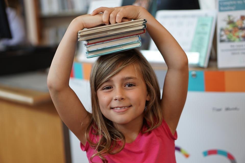 Girl balances pile of books on her head. - Safe Summer Bucket List – 100 Ways to Have Fun This Summer While Social Distancing