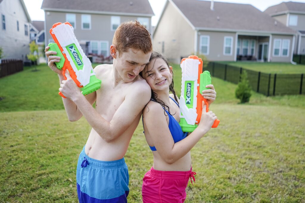 Kids stand back to back with water-guns. Water gun games are the perfect way to beat the heat and cool off outside. All you need is water and your choice of soaker. From a simple water blaster to big super soaker there are endless choices. 