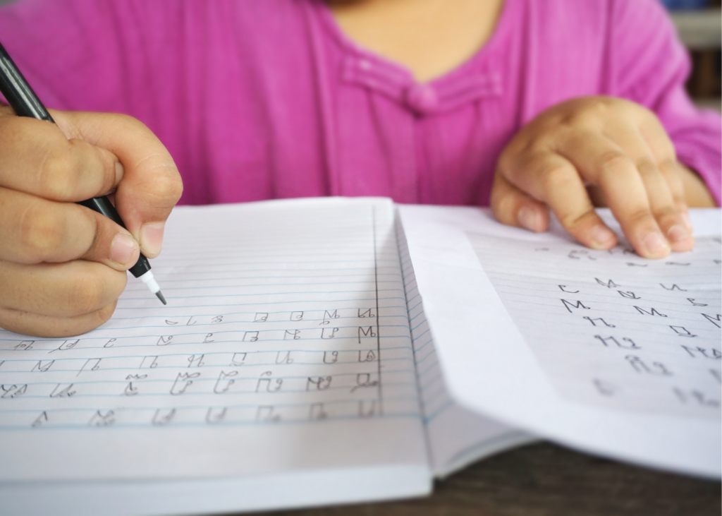 Close-up image of girl practicing cursive. Cursive and calligraphy are not often taught in schools anymore so summer is the perfect time to learn this timeless skill. You can print off practice pages online or use a workbook like this one. - Safe Summer Bucket List – 100 Ways to Have Fun This Summer While Social Distancing