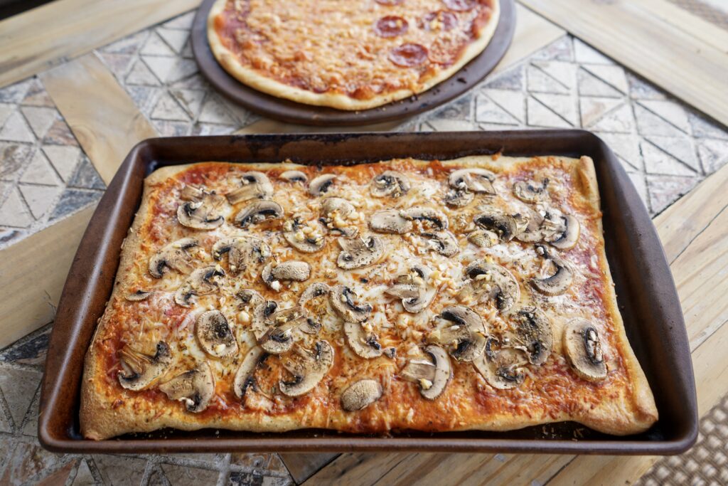 Pan of homemade pizza. Skip the pizza delivery and make your own from scratch instead including the dough! Everyone can take a turn tossing and putting on own tomato sauce, cheese, and toppings. 