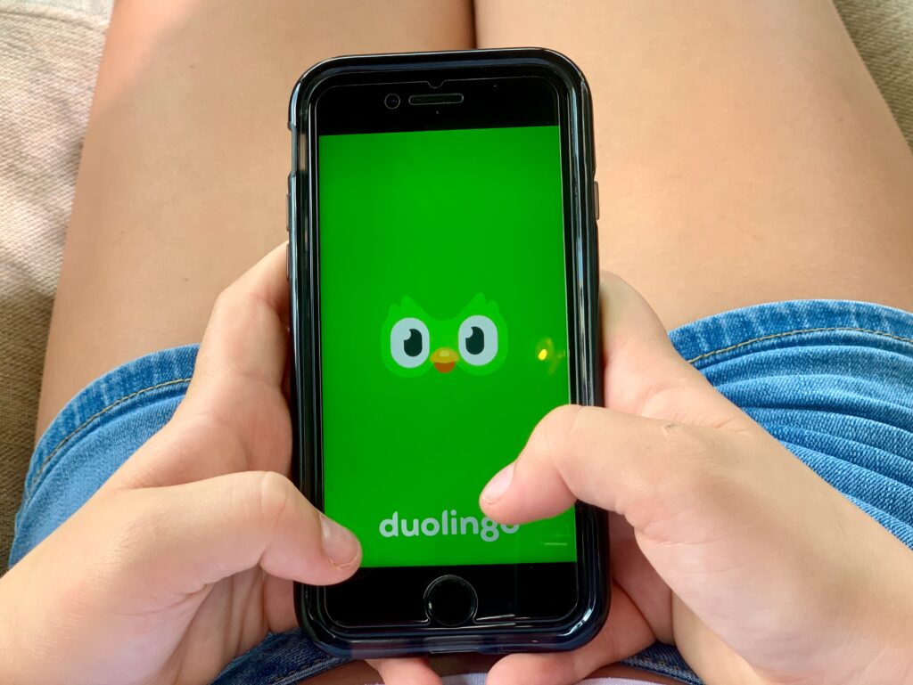 Girl plays Duolingo app on phone. Challenge yourselves this summer to learn a new language! - Safe Summer Bucket List – 100 Ways to Have Fun This Summer While Social Distancing