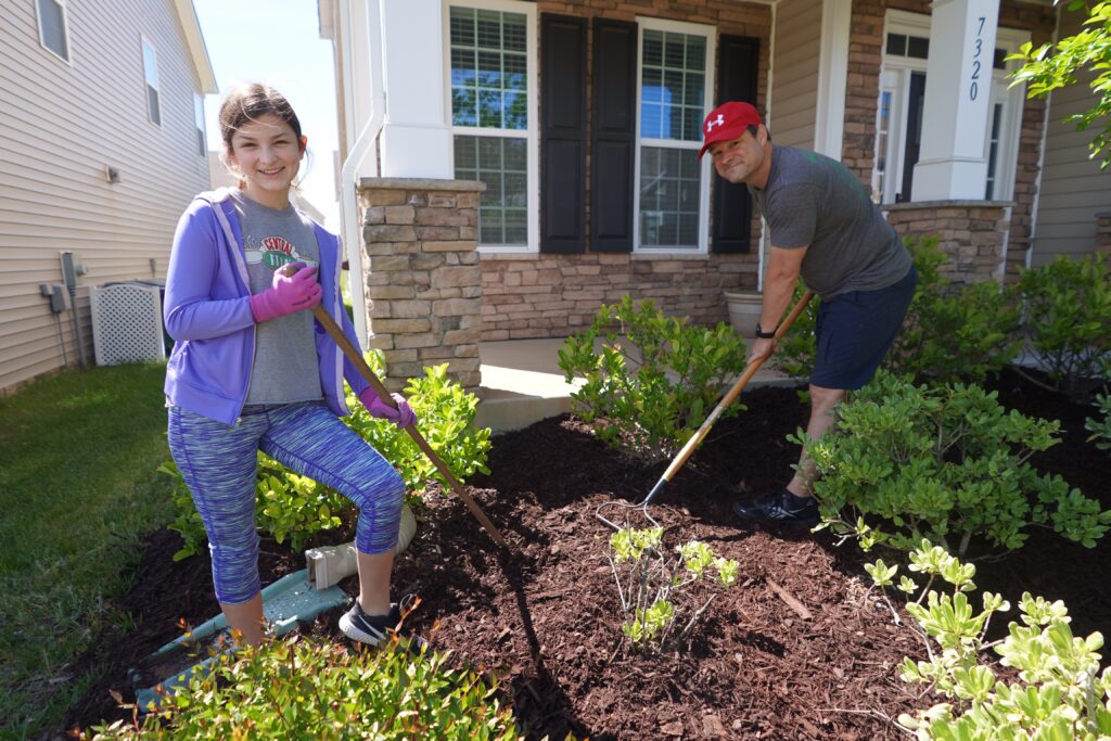 Father and daughter spread mulch in their lawn. Take the opportunity to tackle a big home improvement project together. Whether its adding a patio extension, landscaping your yard or finishing your basement think of ways to involve everyone in the family in the endeavor. 