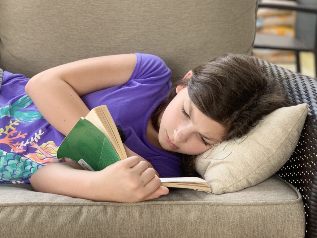 Girl reading a book while lounging on a couch. There’s nothing that opens up new worlds and ideas quite like a good book. Set aside some time every day for quiet reading.