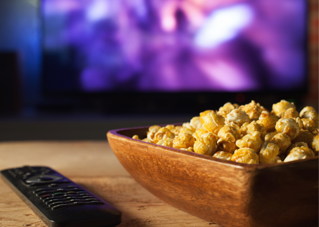 Bowl of popcorn and remote on coffee table with television in background. Take a walk down memory lane by watching old family home videos. Our kids love seeing themselves as toddlers and think it's hysterical how much we, as their parents have changed.